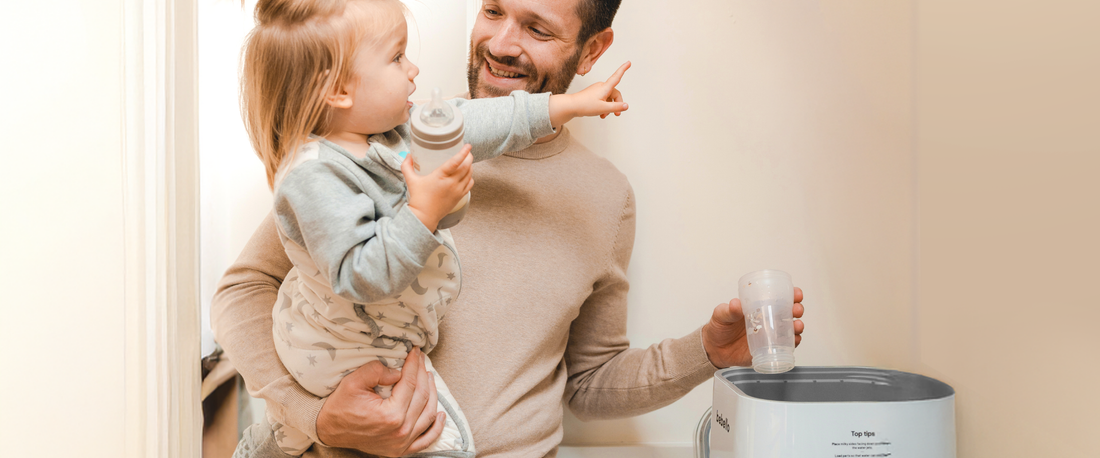 Dad holding baby and putting baby bottles into bottle washer