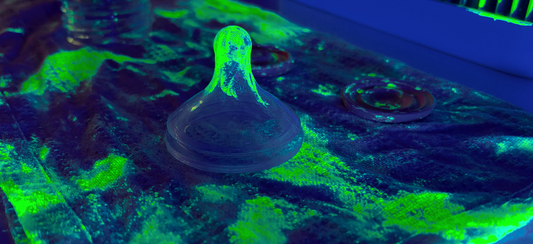 a tea towel with baby bottle parts glowing with bacteria under ultraviolet light
